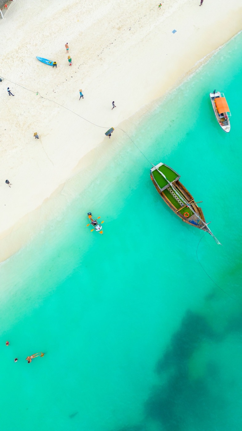 Boat on turquoise water off a white Zanzibar beach, seen from above
